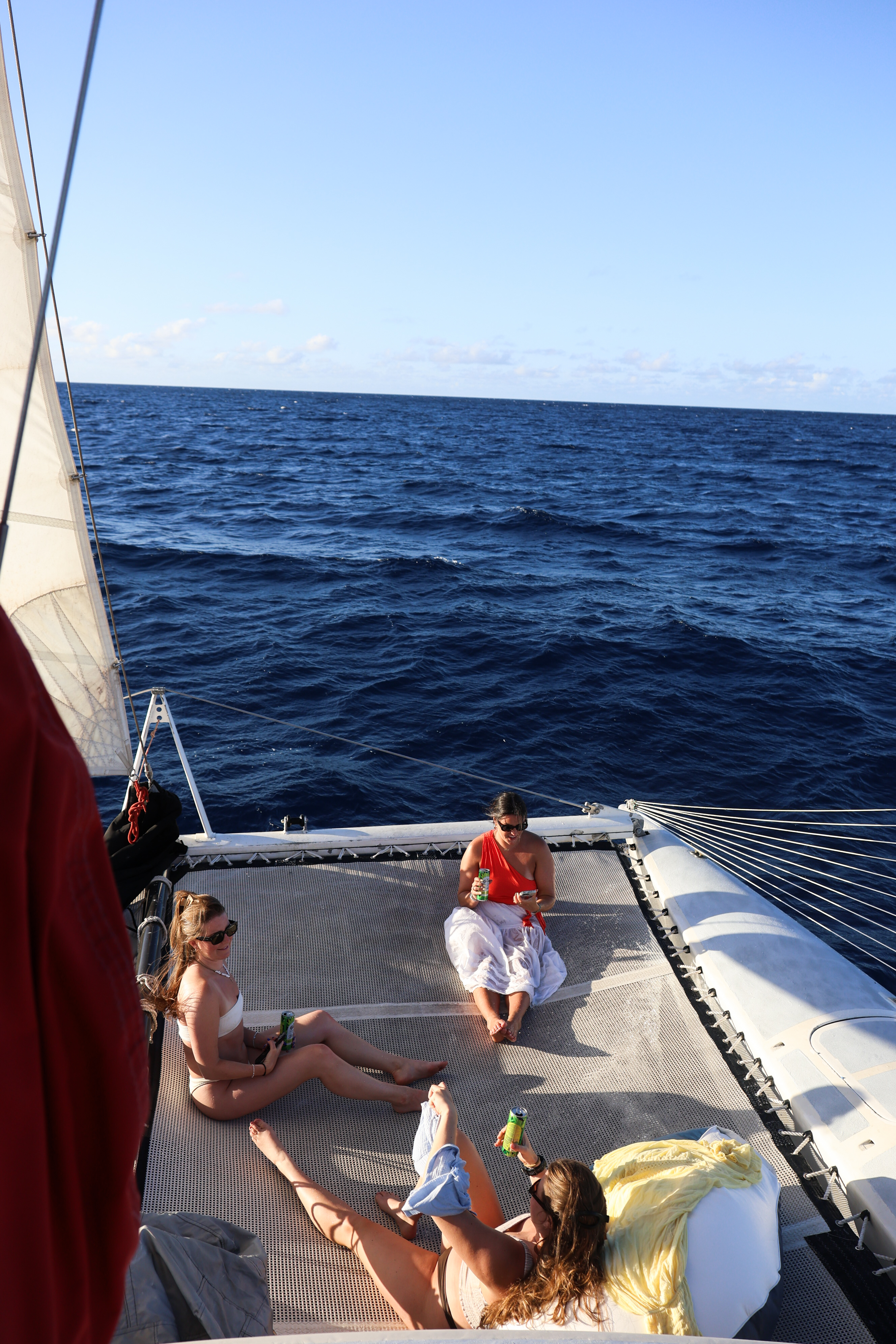 Three women relaxing and drinking on a catamaran trampoline deck over the deep blue ocean.